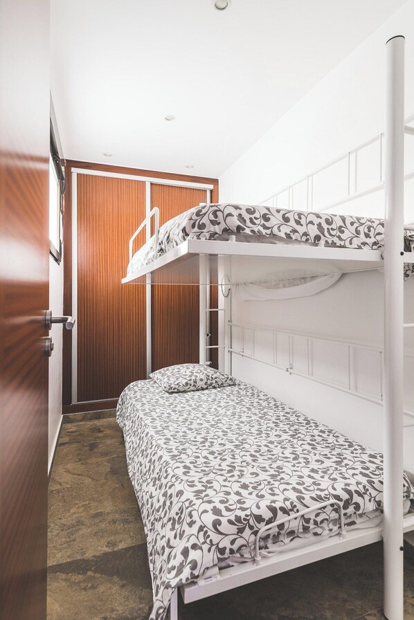 A bunk bed room with a patterned bedspread, a wooden wardrobe, and a door.