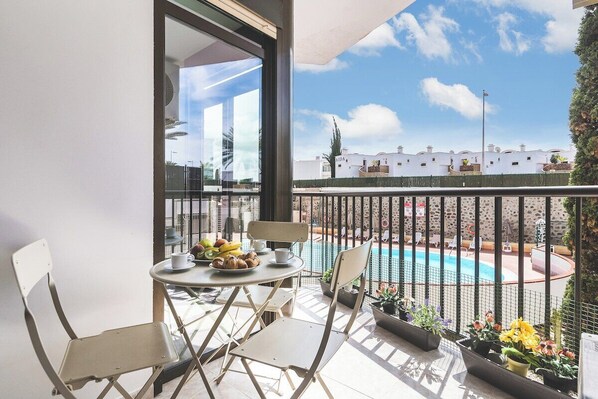 A balcony with a table, chairs, and a view of a swimming pool and buildings. - Home2Book Cozy Apartment Playa del Inglés (Playa del Ingles)