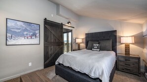 Une chambre à coucher avec un grand lit, un banc, une porte en bois et un tableau au mur.