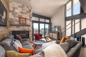 Una sala de estar moderna con chimenea de piedra, un sillón rojo y un amplio ventanal con vista a la ciudad.