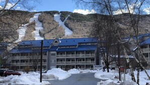 A hotel with a mountain view, a parking lot, and snow-covered ground. - B213 - Loon Mountain Resort Studio with Pool, Hot Tub & Full Kitchen (Lincoln)