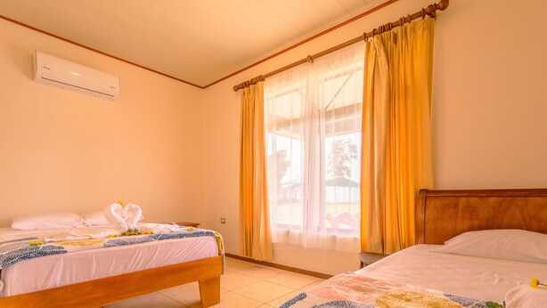 A hotel room with two beds, a wooden headboard, a window with yellow curtains, and an air conditioning unit on the wall. - NOMADS IDEAL PROPERTY 5 MINUTES FROM LA FORTUNA (la fortuna)