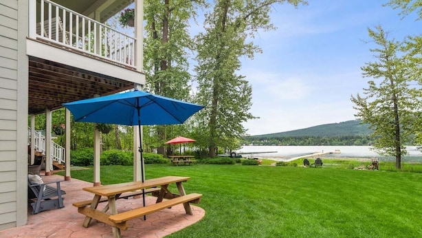Un patio con mesa de picnic y sombrilla, un área de estar cubierta y vista a un lago.