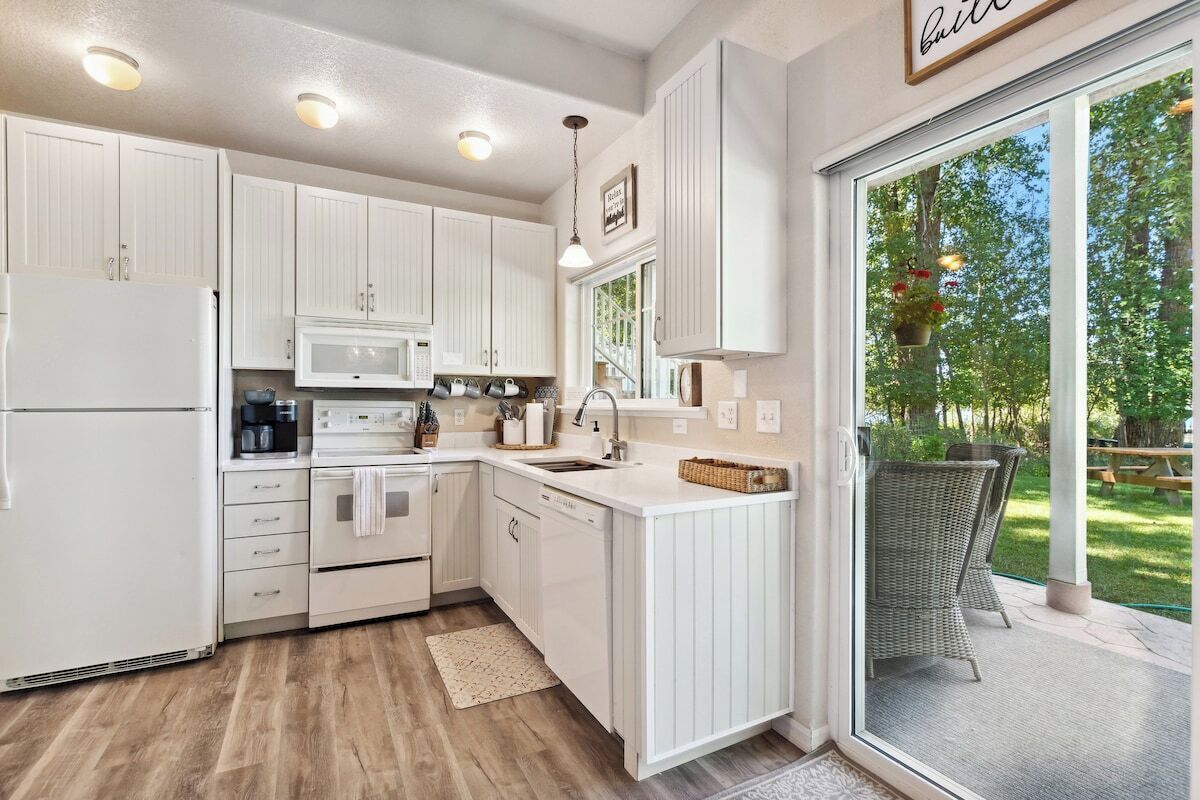 A modern kitchen with white cabinetry, a built-in microwave, and a large window overlooking a garden.