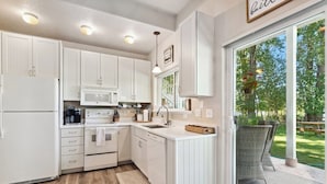 Una cocina moderna con armarios blancos, microondas integrado y un amplio ventanal con vistas a un jardín.