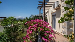 Een balkon met roze bloemen, een pergola en uitzicht op de bergen.