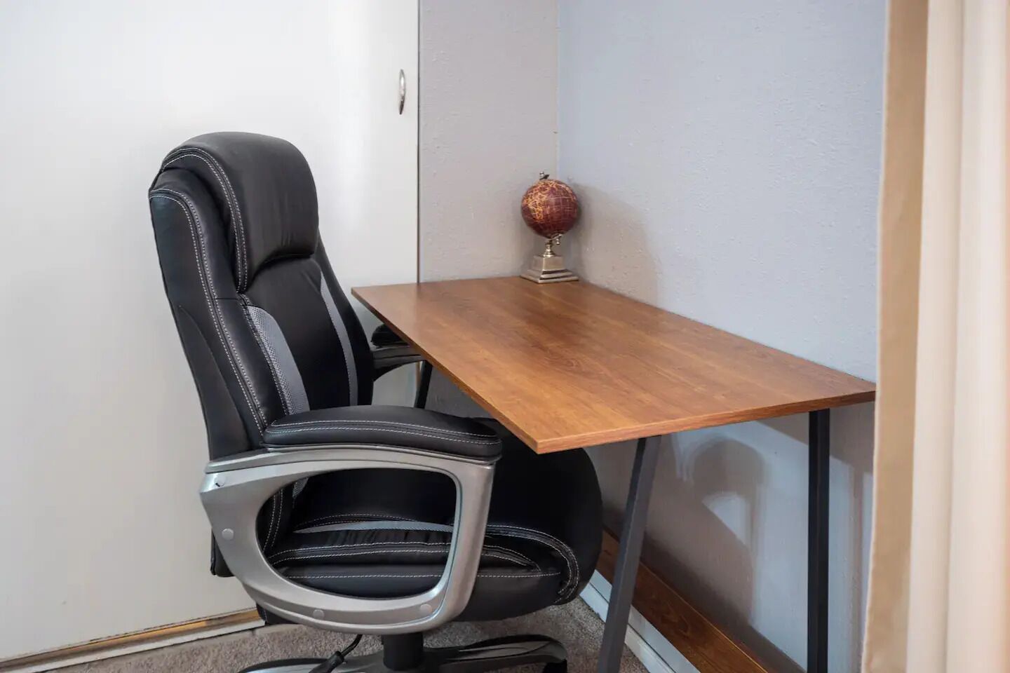 Un bureau d’angle avec un fauteuil en cuir noir, une table en bois et un globe terrestre décoratif.