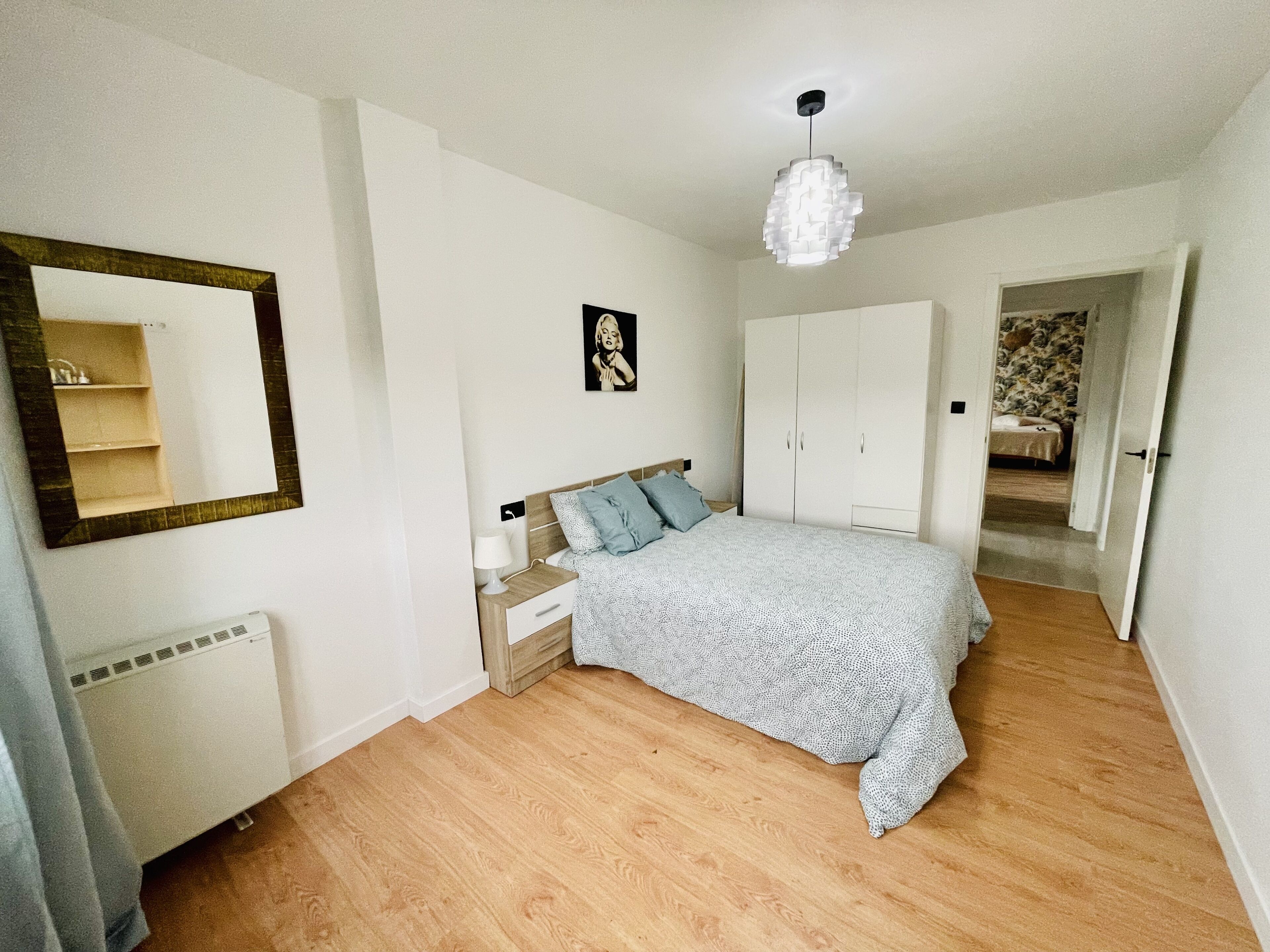 A bedroom with a bed, a nightstand, a mirror, a wardrobe, and a hanging light fixture.