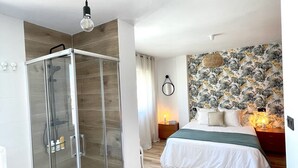 Un dormitorio con ducha de vidrio, cama con una manta verde y pared con estampado floral.