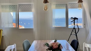 Un comedor con una mesa dispuesta para dos, un centro de mesa con flores y vistas al mar a través de amplios ventanales.