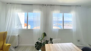 Una habitación con dos ventanas, una silla amarilla, una mesa de madera y una planta en maceta.