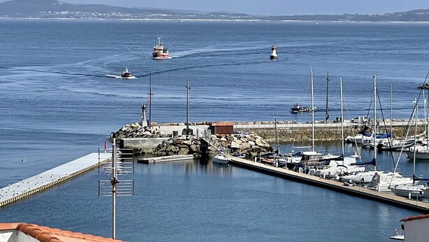 Un puerto deportivo con barcos amarrados, un faro y un rompeolas rocoso.