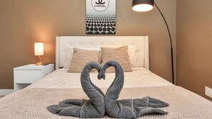 A neatly made bed with a swan towel decoration, a white headboard, a lamp, and a Chanel logo on the wall. - Stylish Townhouse in Central Houston (Houston)