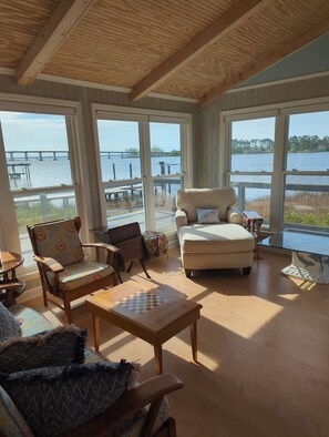 A spacious room with large windows overlooking a body of water and a pier. There are multiple seating options including a sofa, chairs, and a small table. - Rivendock Rookery II: Waterfront Home w/Dock & Stunning Views (Oriental)