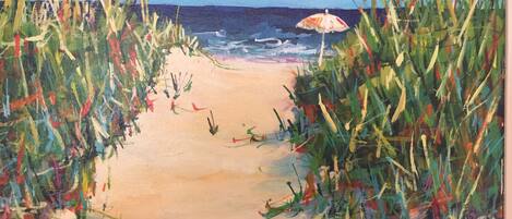 A beach pathway with tall grass on either side and a beach umbrella in the distance.