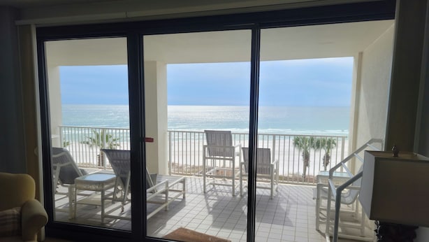A room with a large sliding glass door leading to a balcony with beach views.