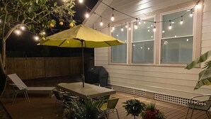 Une terrasse extérieure avec une table et des chaises, un parasol jaune et des guirlandes lumineuses.