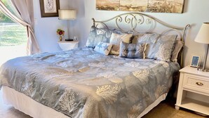 A neatly made bed with a blue and white patterned bedspread, a metal headboard, and a bedside table with a lamp and a framed photo. - Delray Lonepine Estate Guest House (Delray Beach)