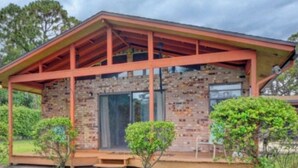 A single-story house with a brick exterior, a wooden porch, and a small front yard with two bushes. - Delray Lonepine Estate Guest House (Delray Beach)