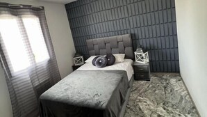A bedroom with a bed, a nightstand, a lamp, and a window with curtains. - Villa festival avignon (Avignon)