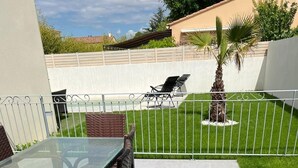 A patio with a glass-top table and wicker chairs, surrounded by a white fence and a well-maintained lawn. - Villa festival avignon (Avignon)