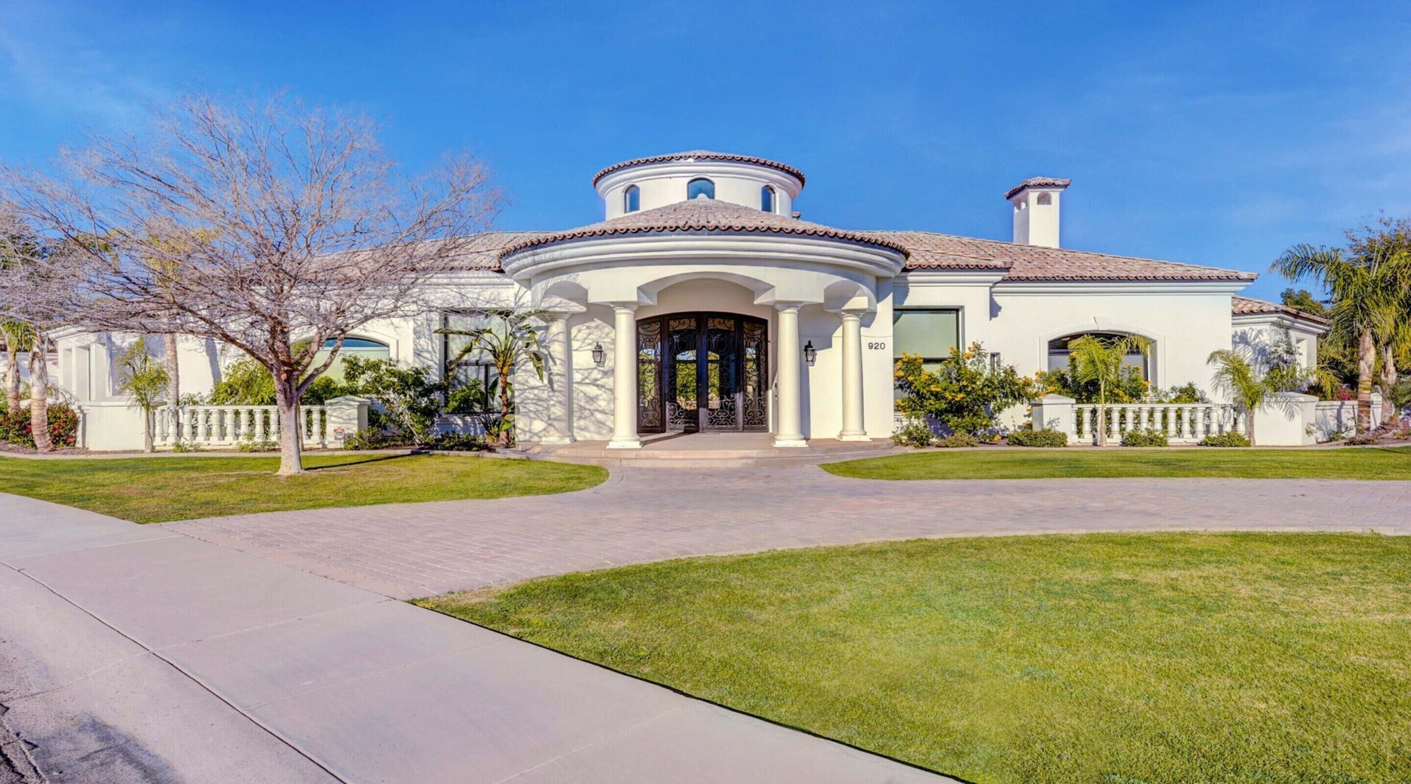 A large, white, two-story house with a circular central section, a tiled roof, and a well-maintained lawn.