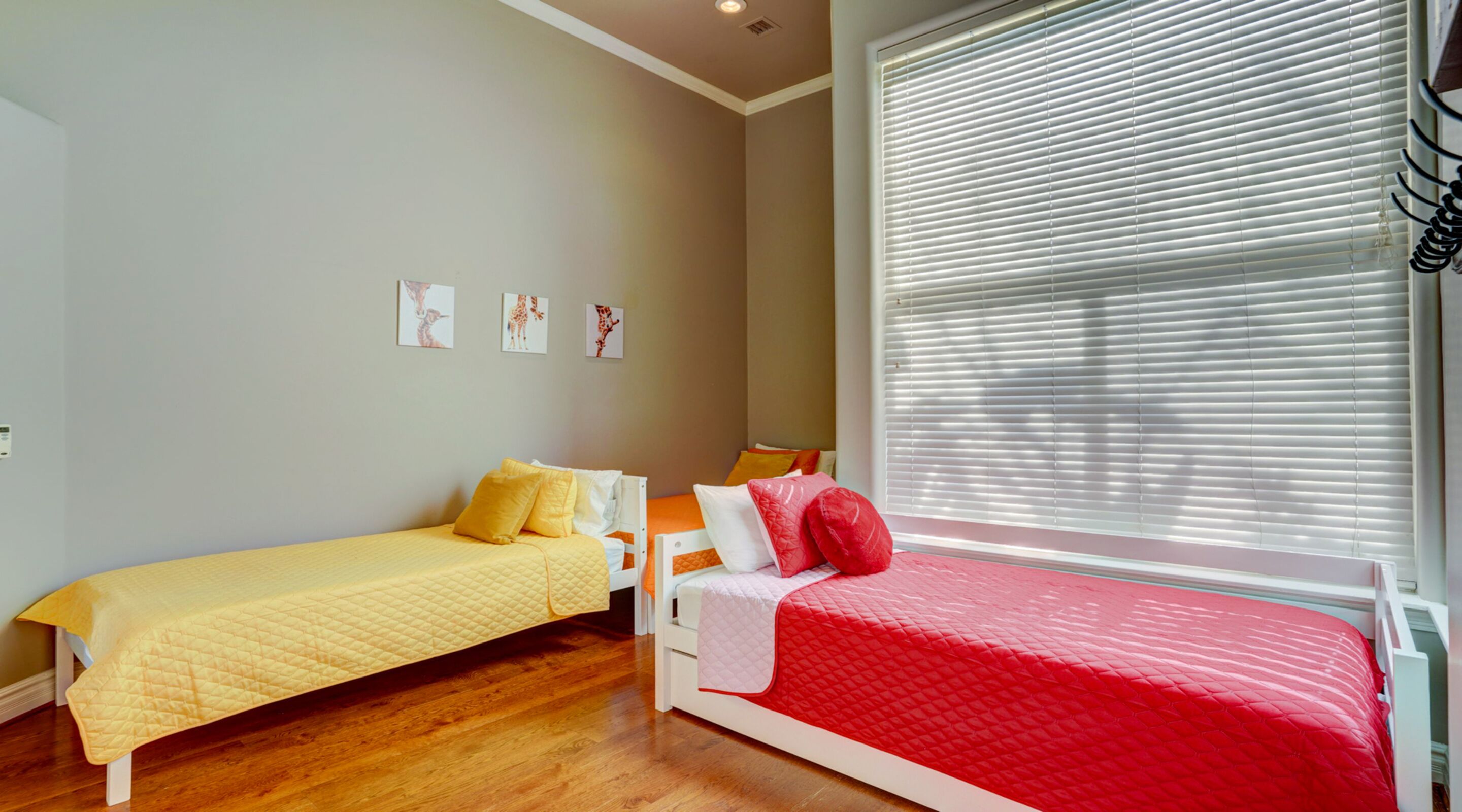 Une chambre avec deux lits, l’un recouvert d’une couvre-lit jaune et l’autre d’une couvre-lit rouge. Trois tableaux encadrés ornent le mur.