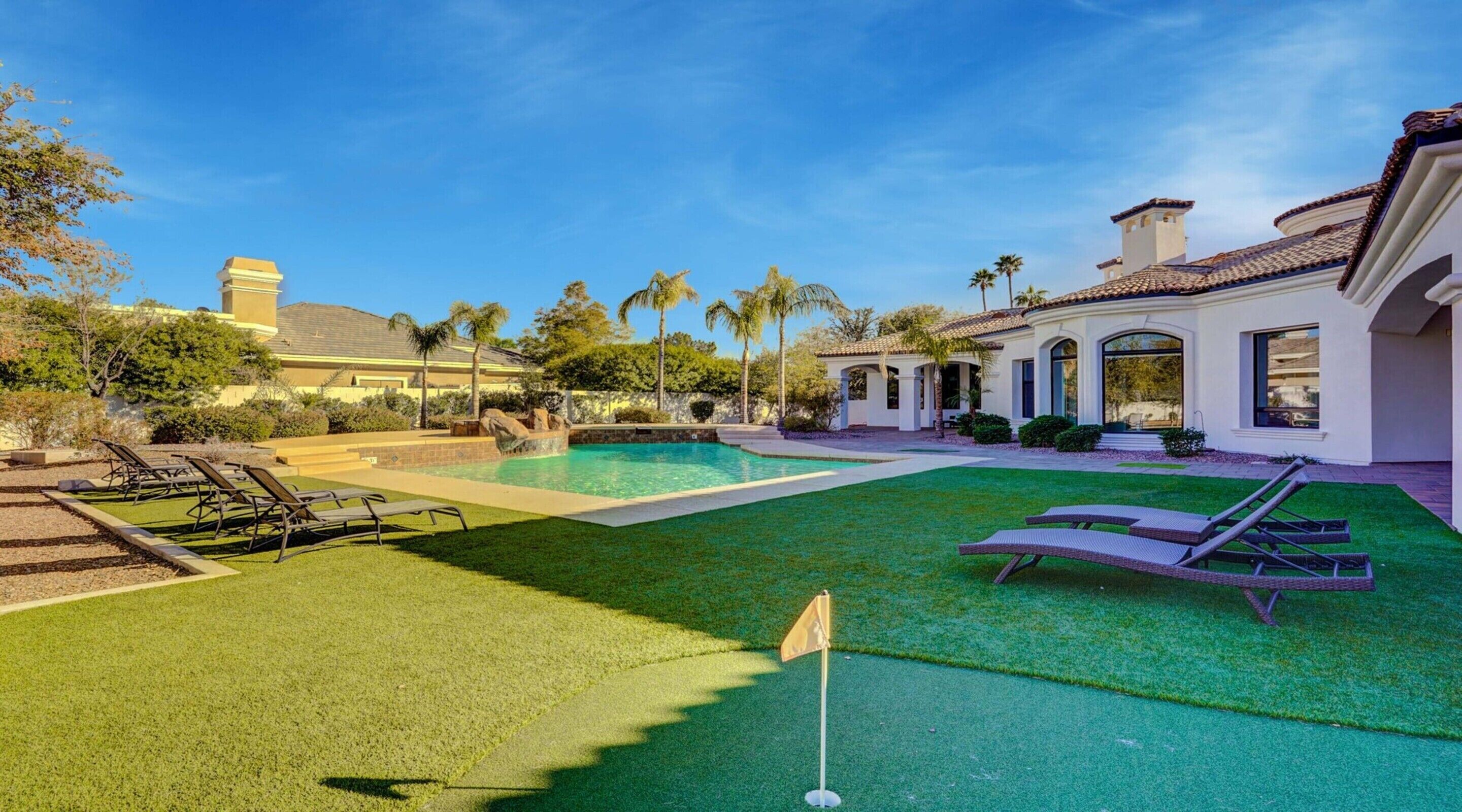 A well-maintained backyard with a swimming pool, artificial turf, and lounge chairs.