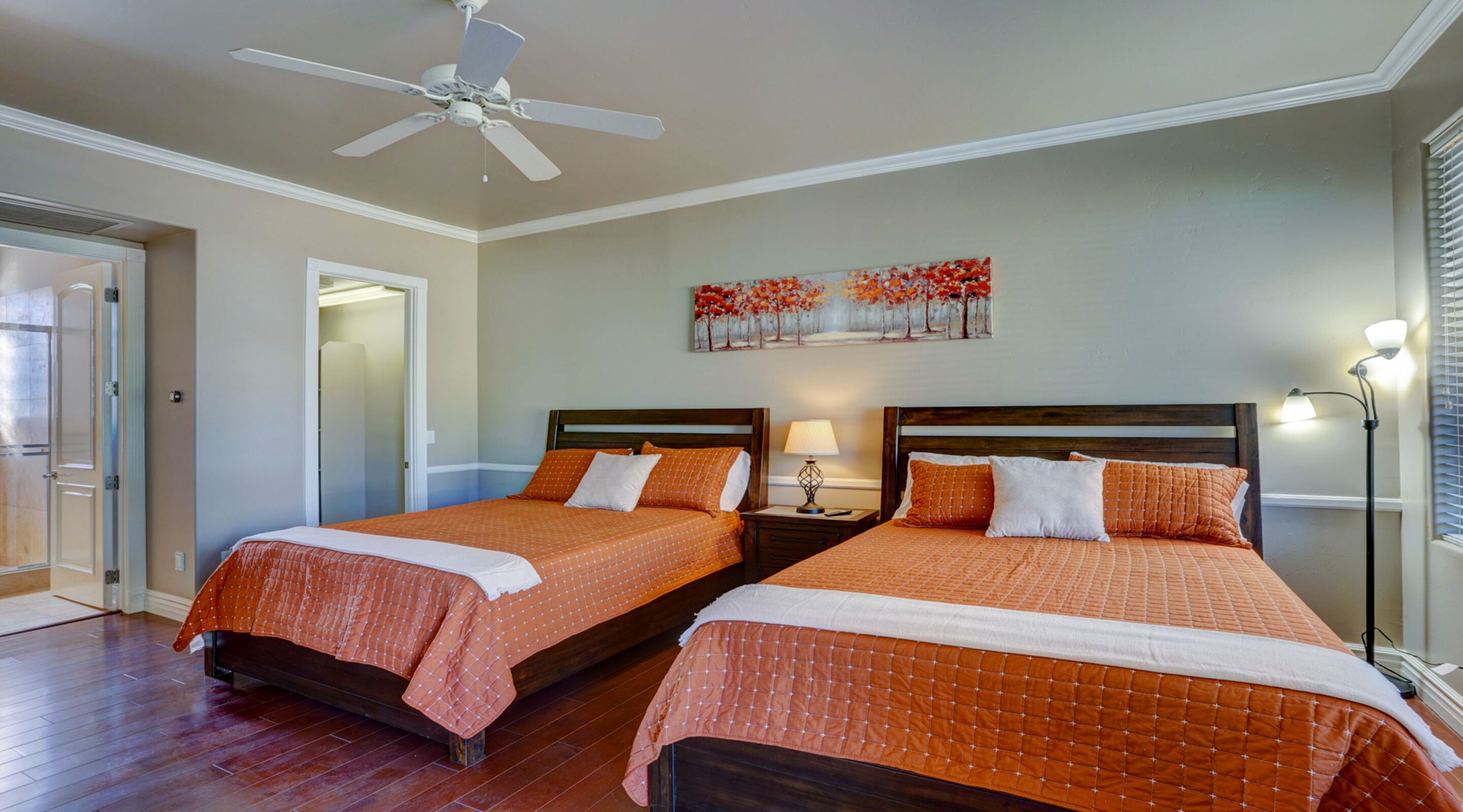 A hotel room with two beds, a ceiling fan, a painting on the wall, and a nightstand with a lamp.