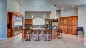 A spacious kitchen with a central island, wooden cabinets, stainless steel appliances, and pendant lighting. - Villa del Sol (Tempe)