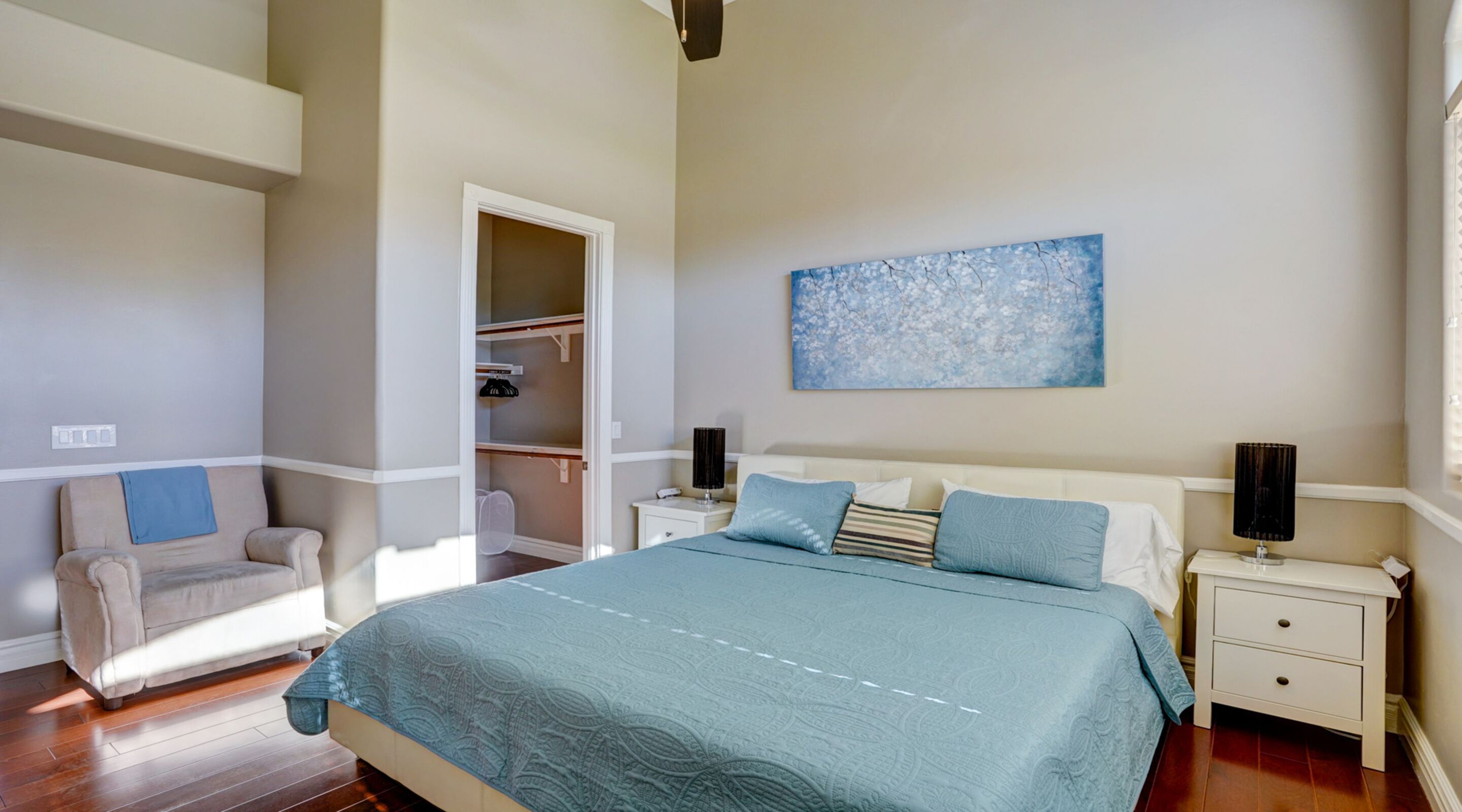 Een slaapkamer met een bed, nachtkastjes, een stoel, een kledingkast en een schilderij aan de muur.