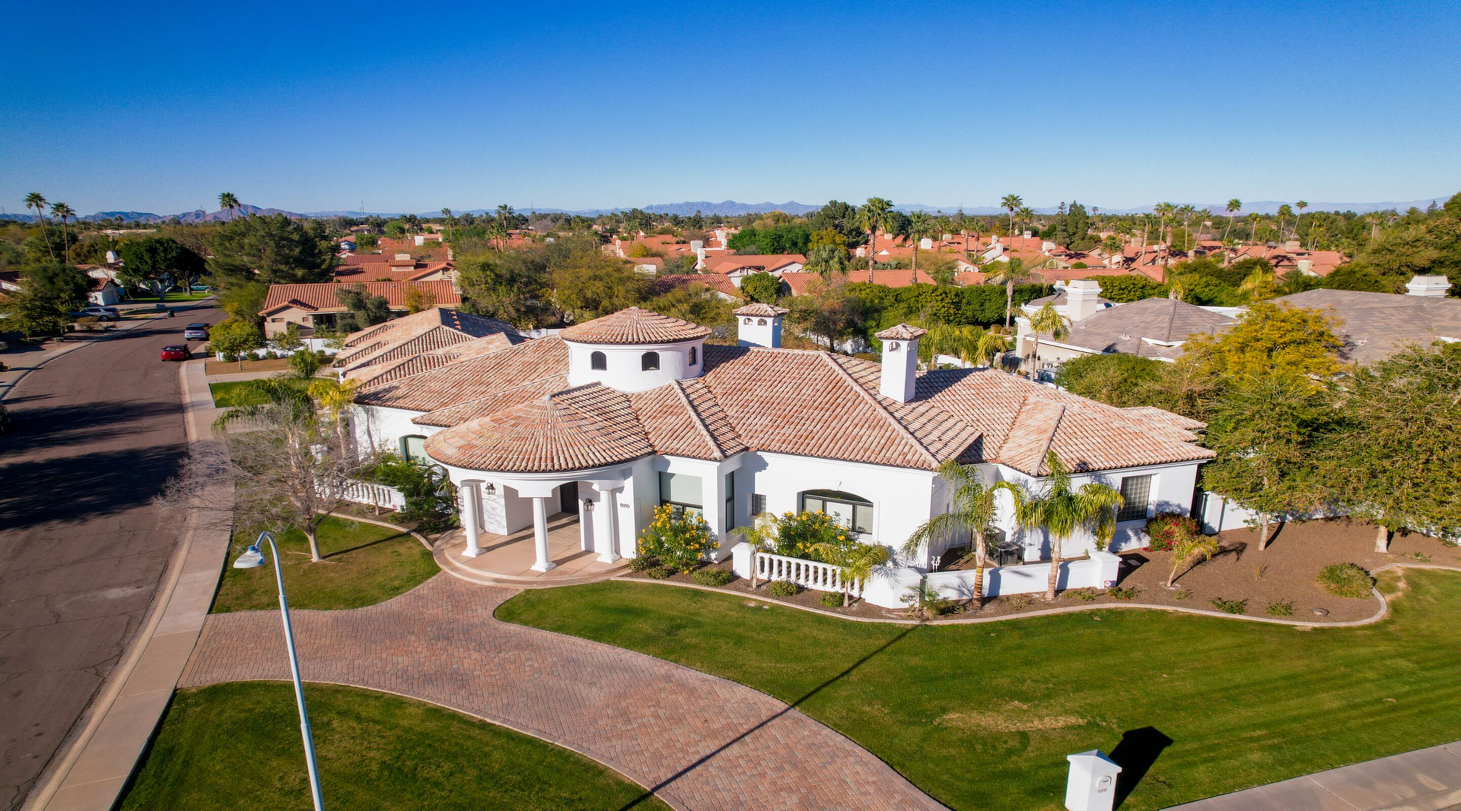 A large, single-story house with a tiled roof, a circular patio, and a well-maintained lawn.