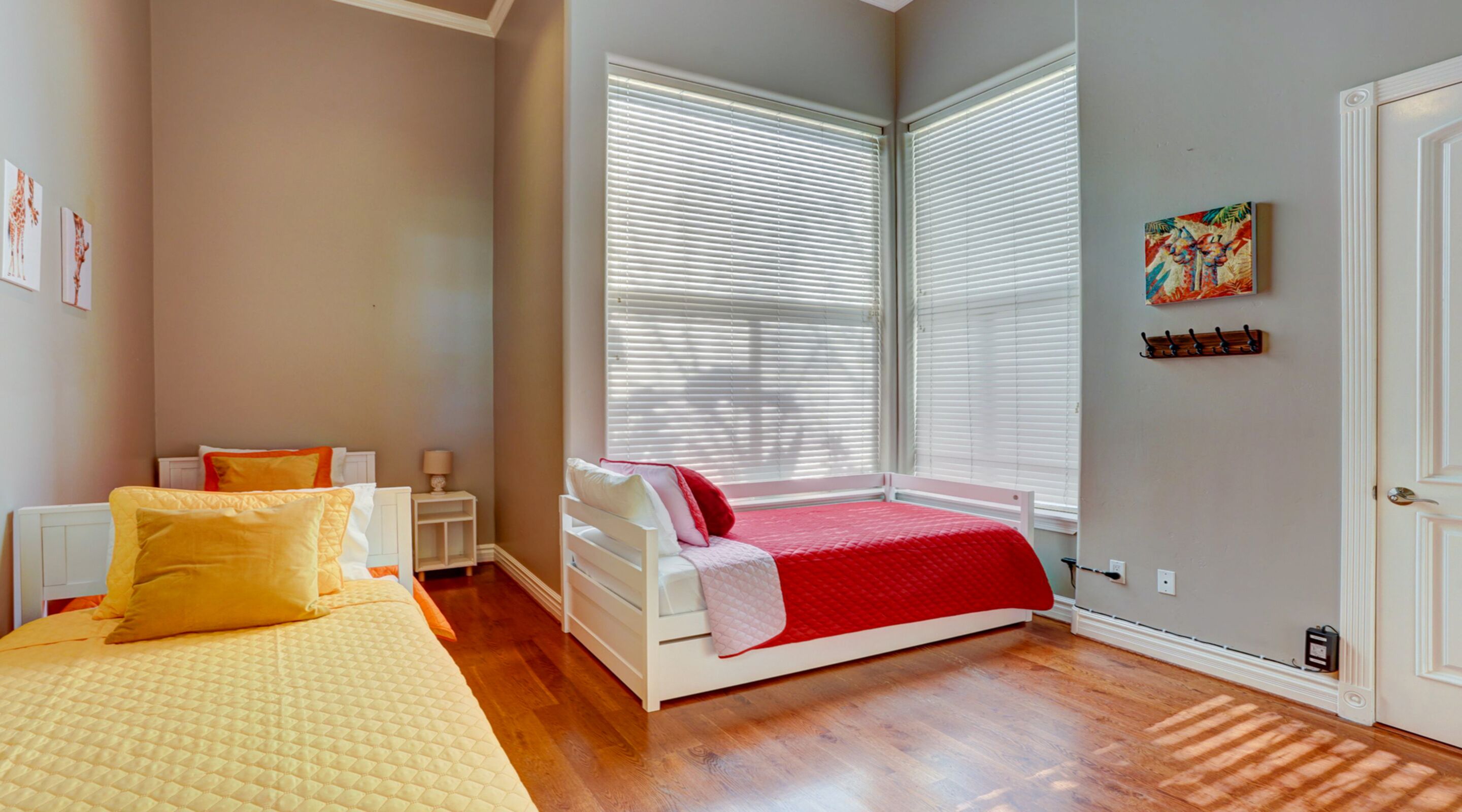 A bedroom with two beds, a window with blinds, a radiator, and a door.