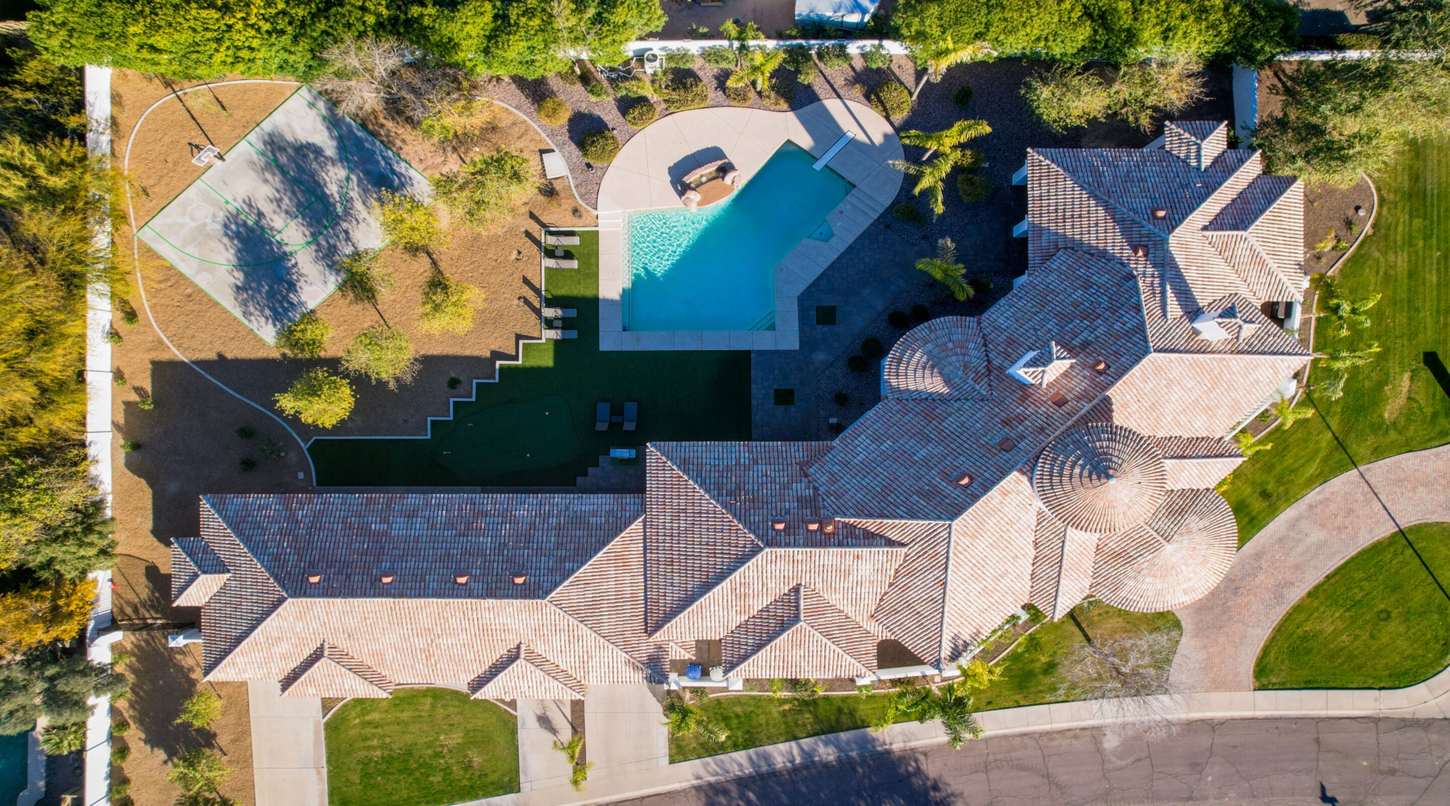 An aerial view of a residential property with a swimming pool, multiple patios, and a landscaped garden.