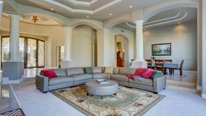 A spacious living room with a large sectional sofa, a round ottoman, and a dining area with a table and chairs. - Villa del Sol (Tempe)