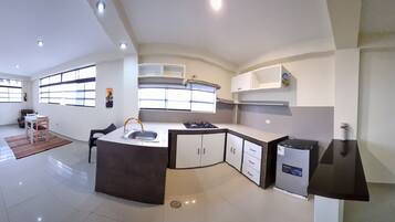 Een koelkast, een waterkoker, kookgerei, borden en bestek, eettafels