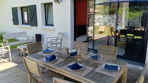 An outdoor dining area with a wooden table set for four, surrounded by chairs.