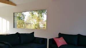 A modern living room with two dark sofas, a coffee table, and a large window with a view of trees.