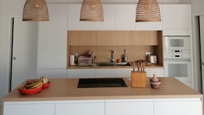 A modern kitchen with white cabinets, a wooden island, and three woven pendant lights.