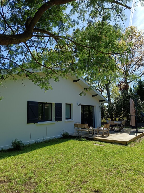 Una casa blanca con un patio, una mesa y sillas, y un árbol grande al fondo.