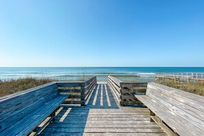 Une promenade en bois qui mène à une plage d’où l’on a une vue dégagée sur l’océan.