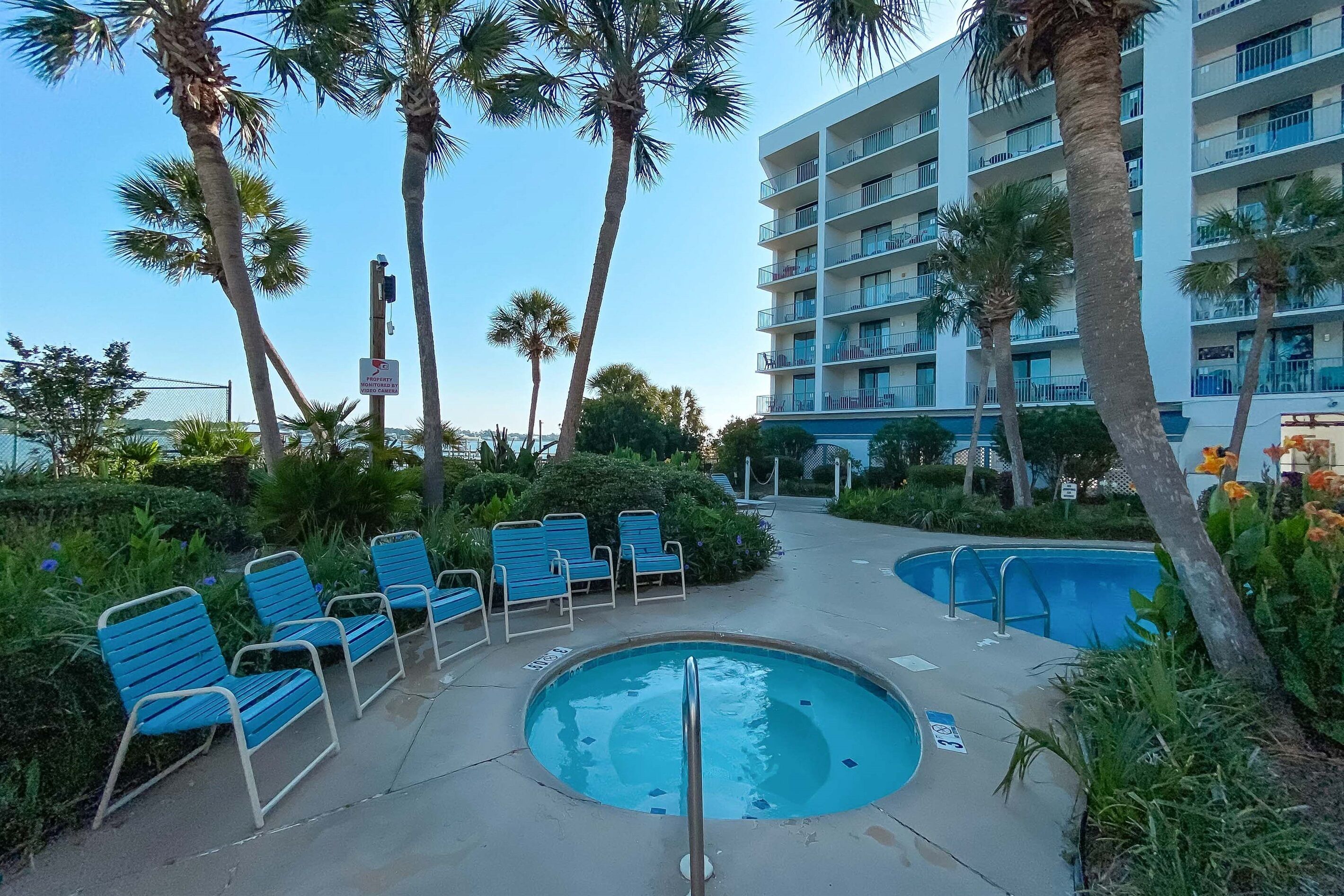 A pool area with lounge chairs, a hot tub, and a multi-story building with balconies.