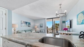 A kitchen with a marble countertop, stainless steel sink, and a chandelier. There are two paintings on the wall and a view of the outdoors through a glass door. - Gulf Shores Surf and Racquet Club 211A | King Bd | Boat Launch |Trailer Parking (Gulf Shores)