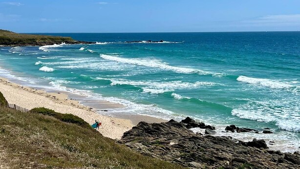 A beach with waves crashing onto the shore, a clear sky, and rocky terrain.