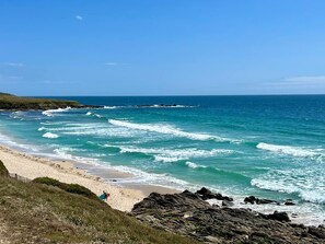 A beach with waves crashing onto the shore, a clear sky, and rocky terrain.