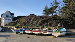 A row of boats parked on a concrete surface near a house with a hill in the background.