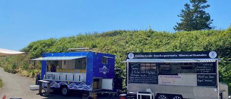Two food trucks parked on a paved area with tables and chairs nearby.