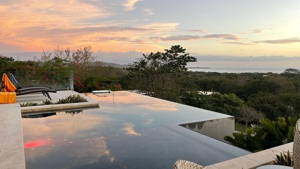 Une piscine à débordement moderne offrant une vue dégagée sur l’océan et le paysage environnant, particulièrement magnifique au coucher du soleil.