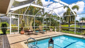 Una piscina al aire libre techada con sillas de descanso y un farol, rodeada de plantas tropicales y palmeras.