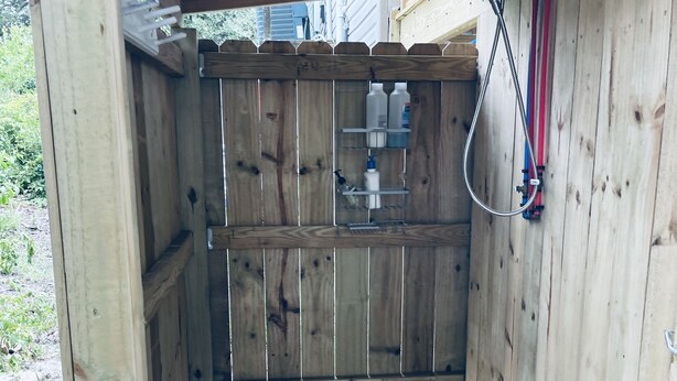 A wooden outdoor shower enclosure with a metal grate floor, a wooden fence, and a metal shelf with bottles. - Unit C, Spirit of Folly, Pet Friendly,  2 short blocks - 100 yards to the beach (Folly Beach)